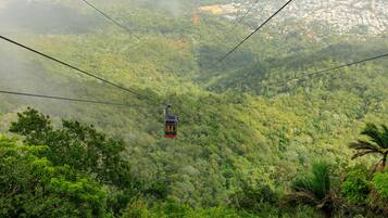 Un teleférico se desplaza por un valle exuberante, verde y con vegetación densa, mostrando una vista distante de un pueblo.