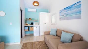 A living room with a beige sofa, a small kitchenette, a microwave, and a ceiling light fixture.