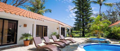 A poolside area with lounge chairs, a swimming pool, and a building with a tiled roof.