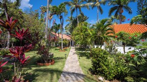 A tropical garden pathway leading to a house with a red-tiled roof.