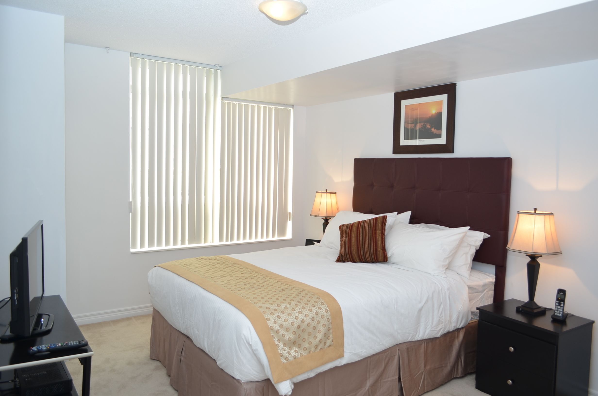 Een netjes ingerichte hotelkamer met een groot bed, twee bedlampjes, een televisie en een raam met zonwering.