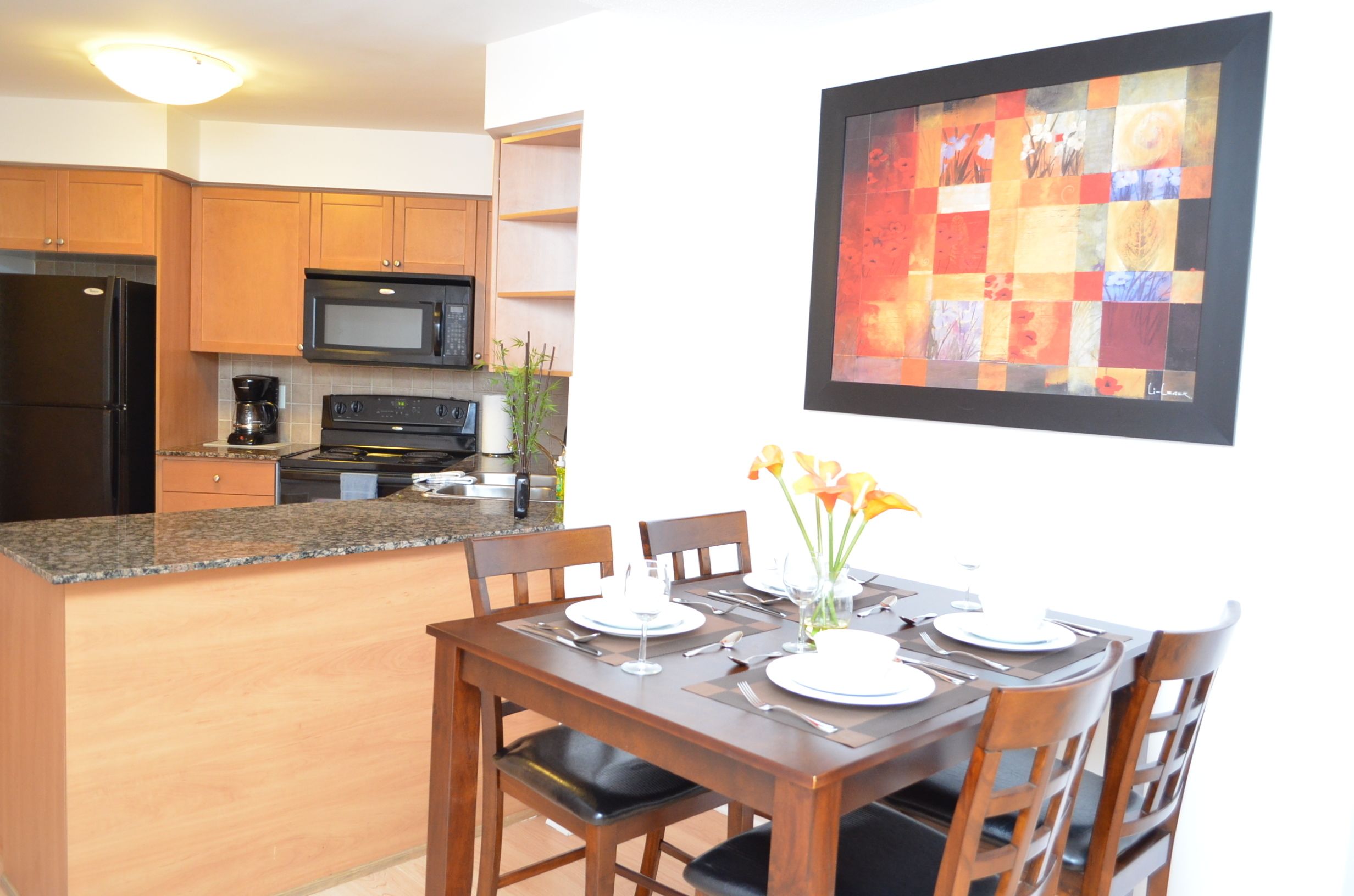 Una cocina moderna con armarios de madera, encimera de granito y comedor con mesa dispuesta para cuatro.