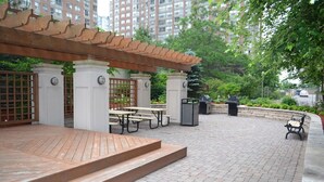 Un espacio al aire libre con patio, piso de madera, mesas de picnic y una estructura de pérgola.