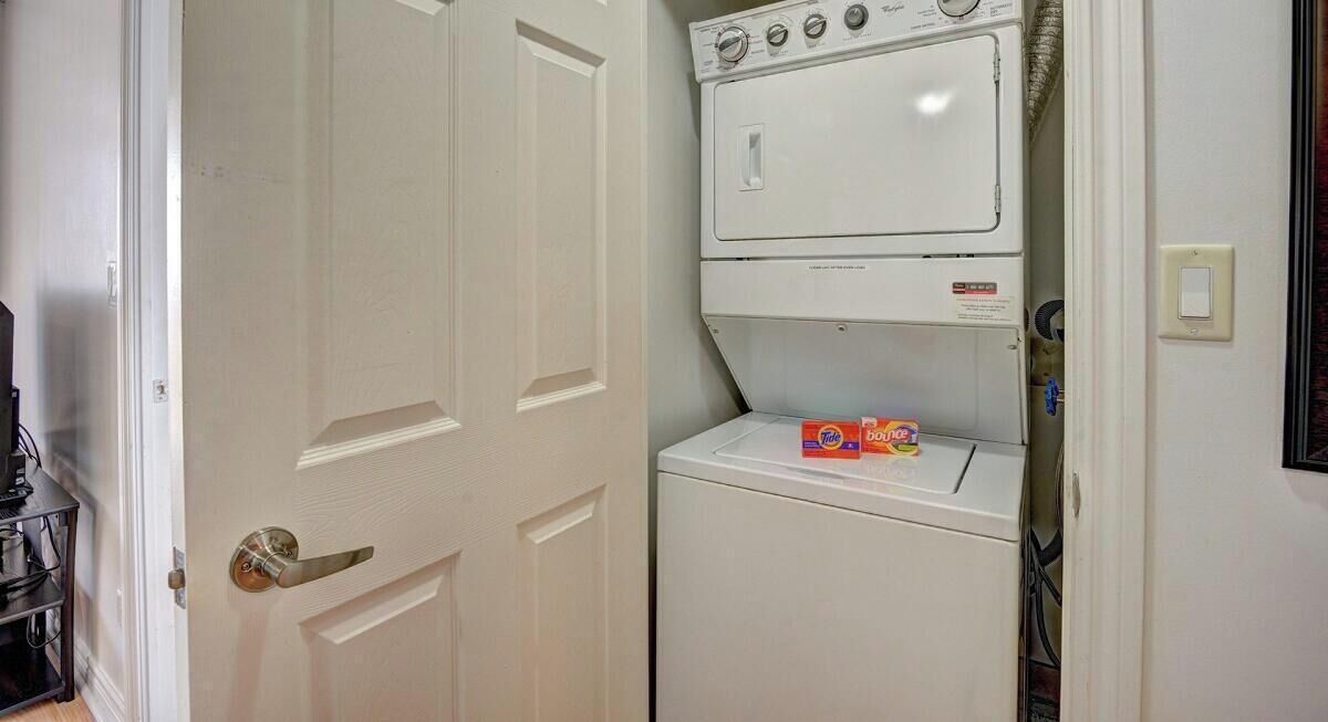 Un cuarto de lavado con lavadoras y secadoras apiladas, una puerta y un estante con detergente.