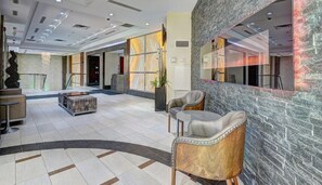 Um hall espaçoso com uma receção em mármore, duas poltronas estofadas, uma mesa de centro e uma parede grande com padrão geométrico.