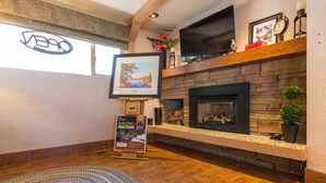 A cozy room with a fireplace, a TV mounted above it, and a framed picture on the wall. - Grama's Inn (Prince George)
