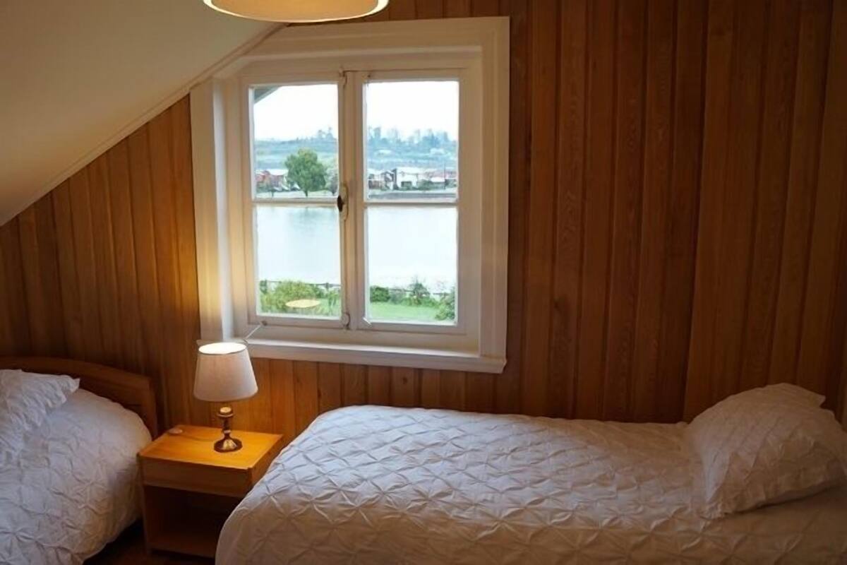 Un dormitorio con dos camas, una ventana con vista a un lago y paneles de madera en las paredes.