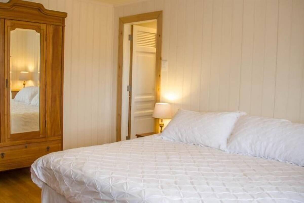 Un dormitorio con un amplio armario de madera, una cama con ropa blanca y una mesita de noche con lámpara.