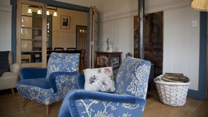 A living room with two blue upholstered chairs, a white sofa, a wicker basket, and a wooden floor. - Hotel Boutique Casa Werner (Llanquihue)