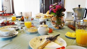 A breakfast table with various food items, a vase of flowers, and kitchen appliances. - Hotel Boutique Casa Werner (Llanquihue)
