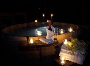 Un jacuzzi con velas y una botella de champán, rodeado de toallas y flores.