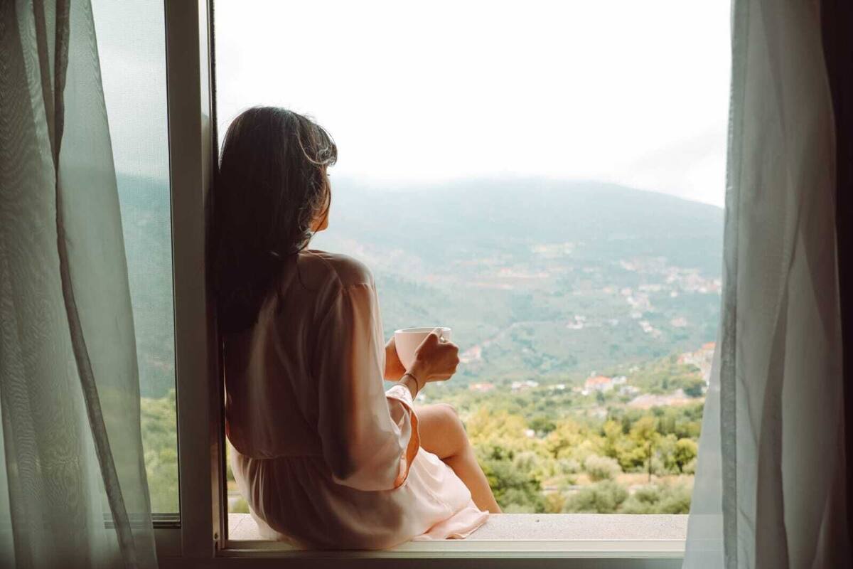Una persona sentada junto a una ventana con vistas al paisaje.