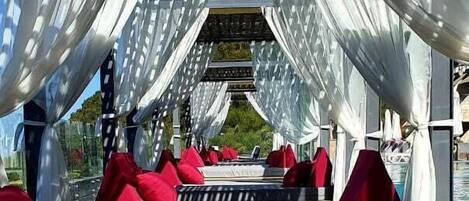 Un espacio de descanso al aire libre con toldos blancos y cojines rojos.