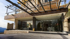 A modern building with a wooden balcony, large glass doors, and a paved entrance area. - Le Tournant Hotel & Resort (Ehden)
