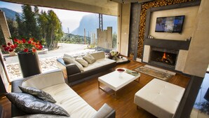 A modern living room with a sofa, ottoman, and coffee table, a fireplace, and a TV mounted on the wall. - Le Tournant Hotel & Resort (Ehden)