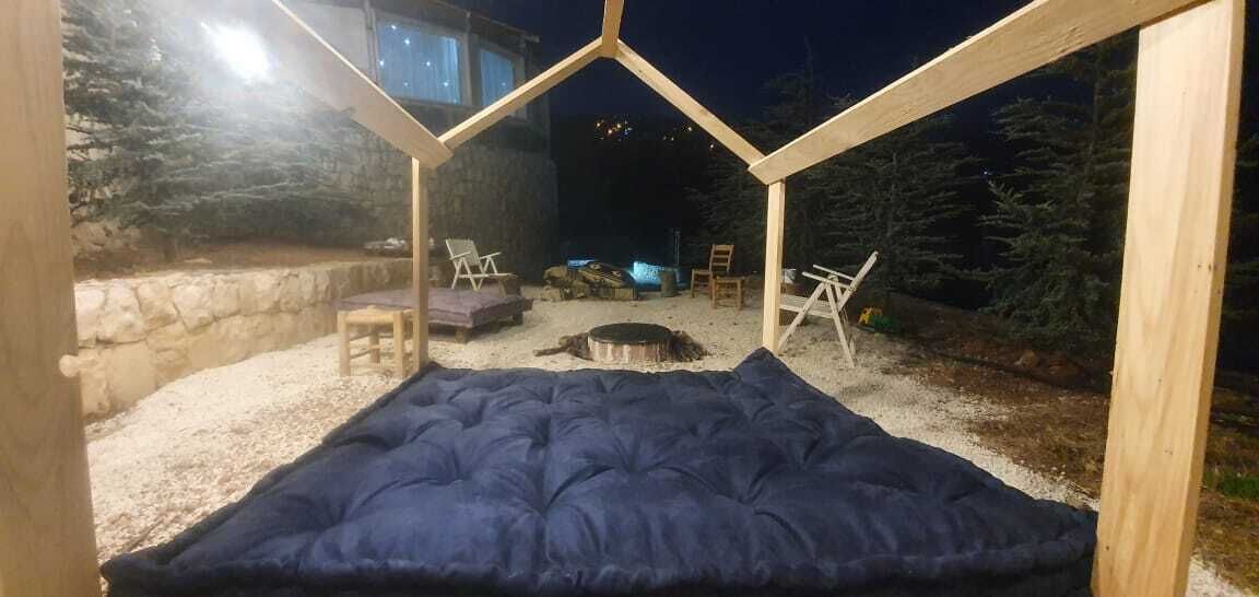 A cozy outdoor sleeping area with a blue mattress, a fire pit, and two chairs.