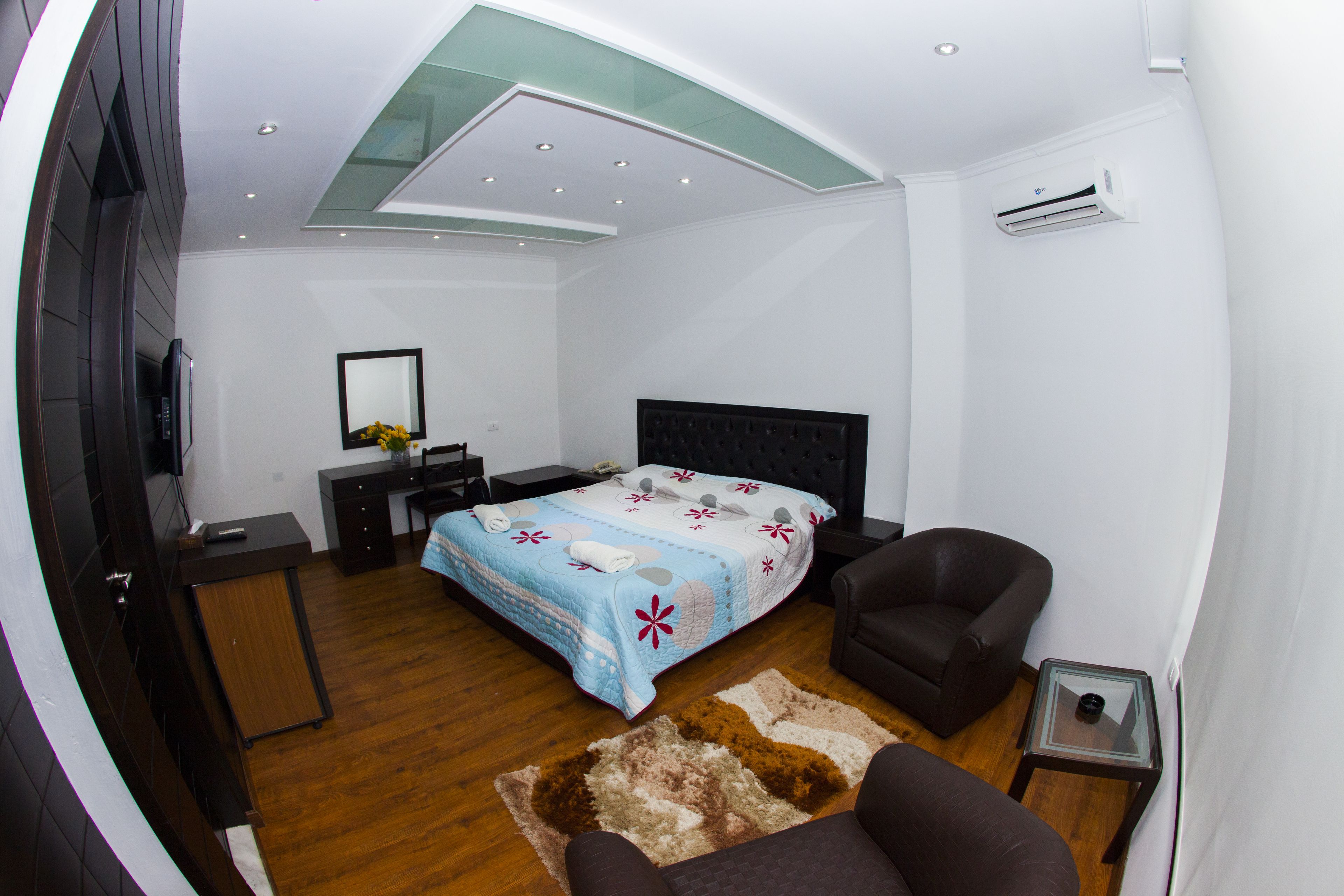 Un dormitorio moderno con cama, sillón, escritorio y televisor.