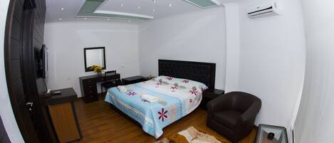Un dormitorio moderno con cama, sillón, escritorio y televisor.