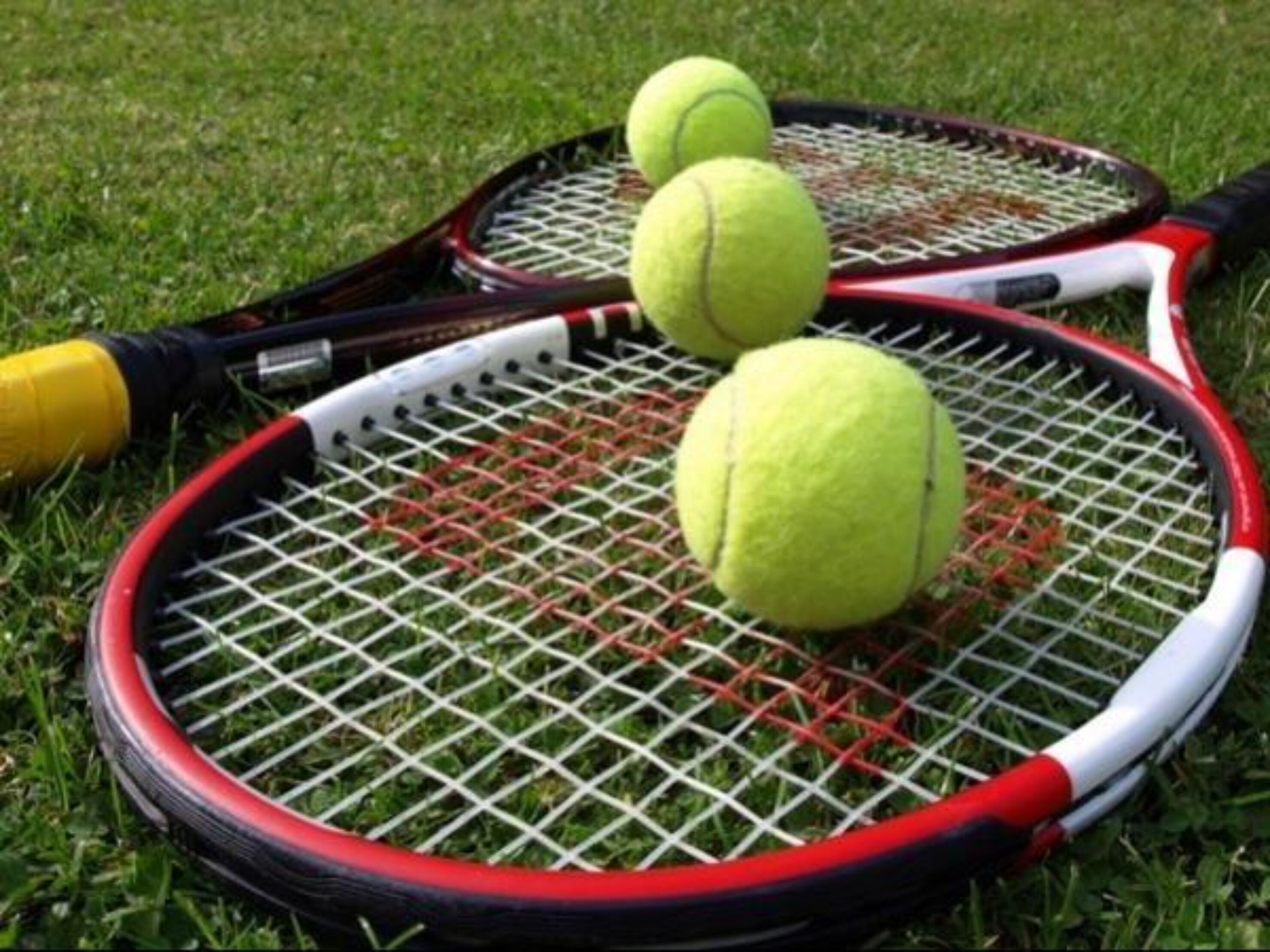 Dos raquetas de tenis y tres pelotas sobre césped.