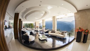 A spacious living area with a modern design, featuring a curved ceiling, large windows with a mountain view, and a variety of seating options. - Le Tournant Hotel & Resort (Ehden)