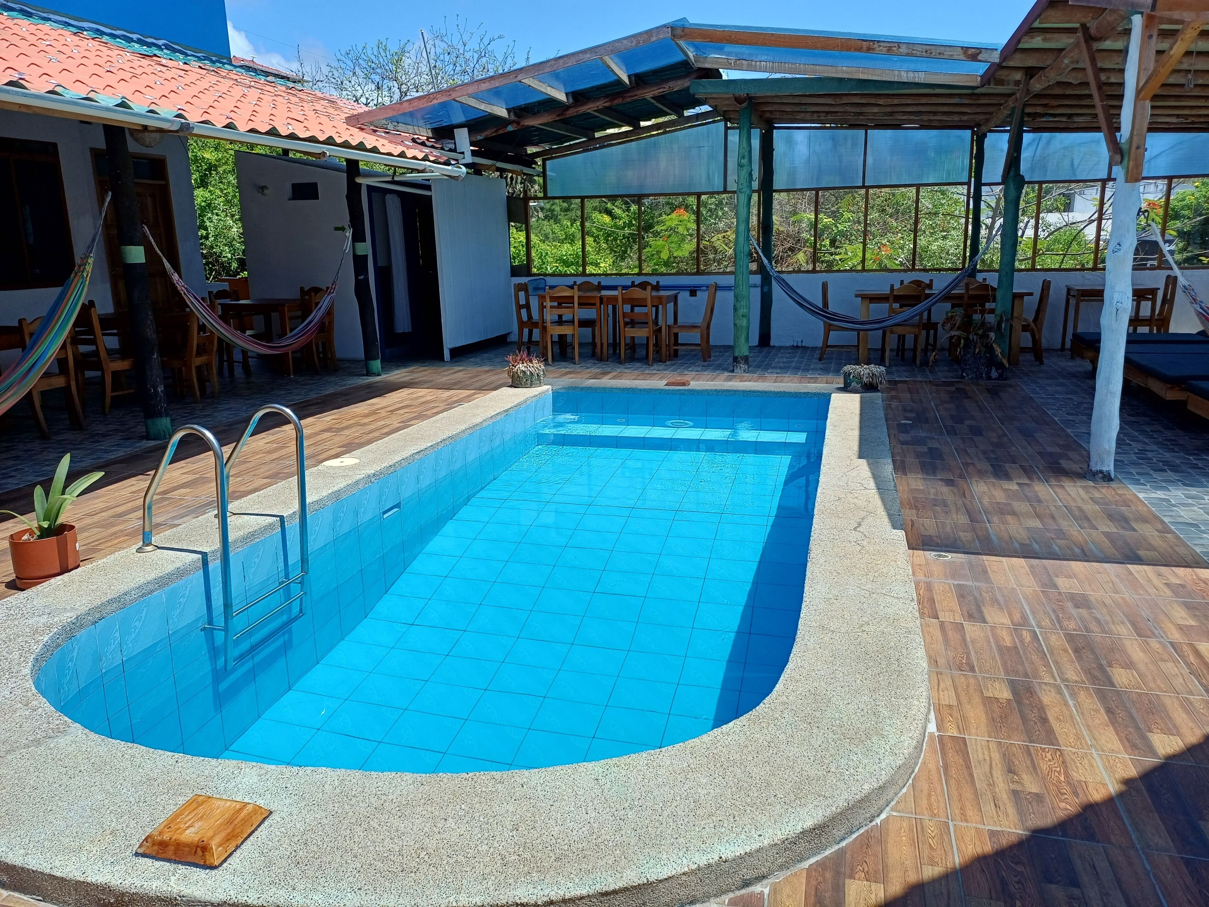 Une piscine avec une terrasse carrelée, des meubles en bois et un espace salon abrité.