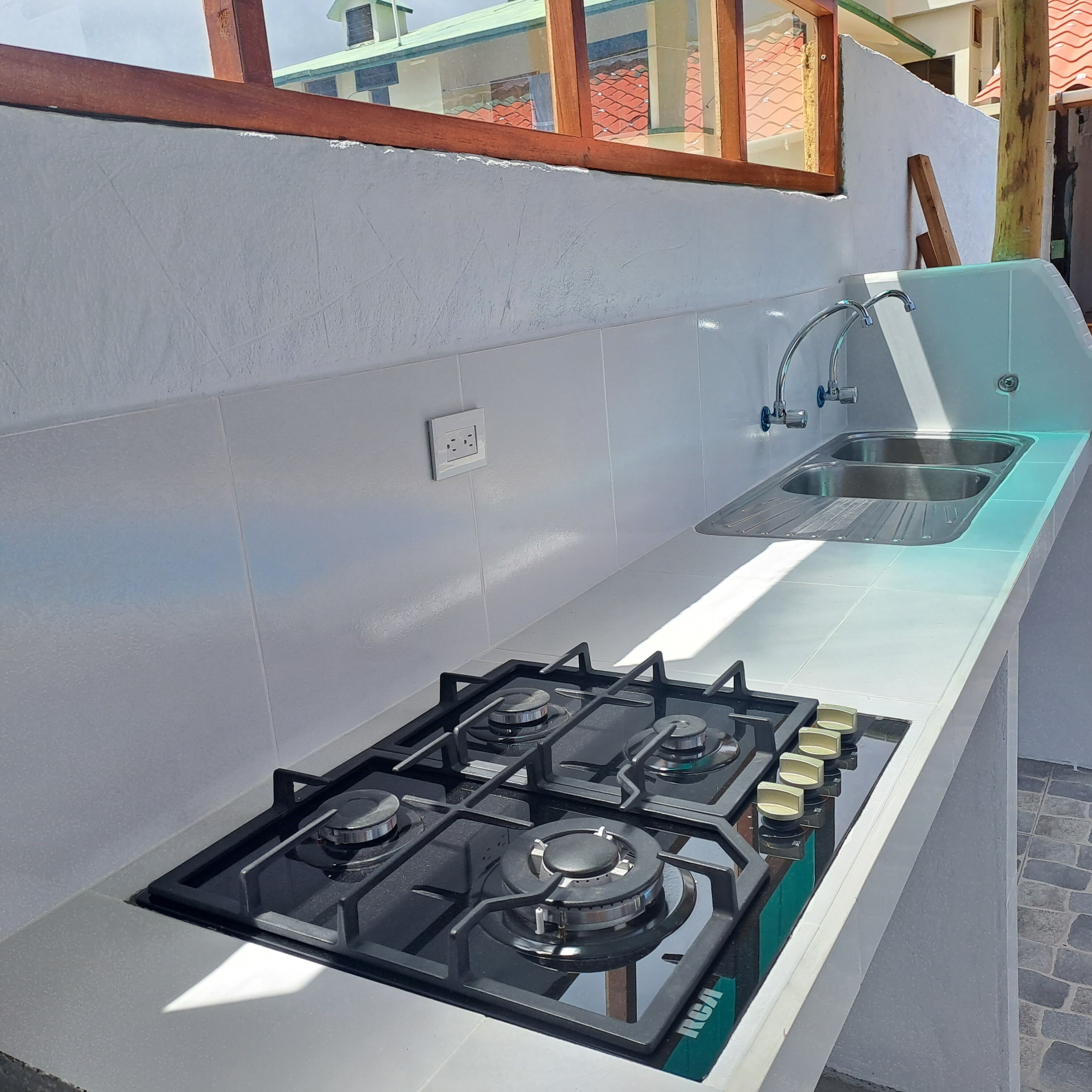 Una cocina moderna con estufa a gas, un lavamanos y una ventana con vista a un tejado de tejas rojas.