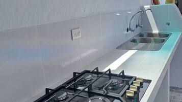 Una cocina moderna con estufa a gas, un lavamanos y una ventana con vista a un tejado de tejas rojas.