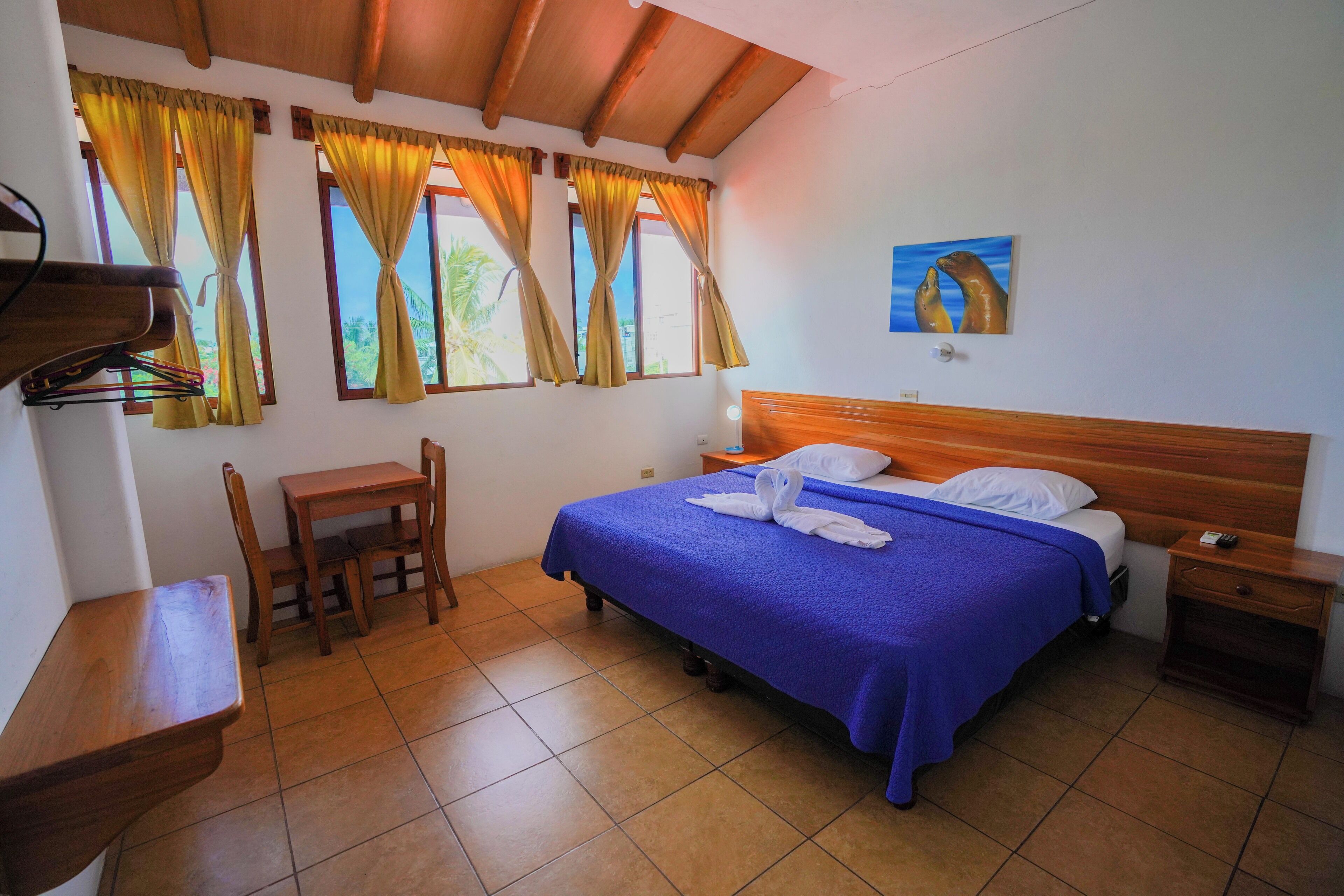 Quarto com cabeceira de madeira, cama com colcha azul, duas almofadas e um quadro na parede.