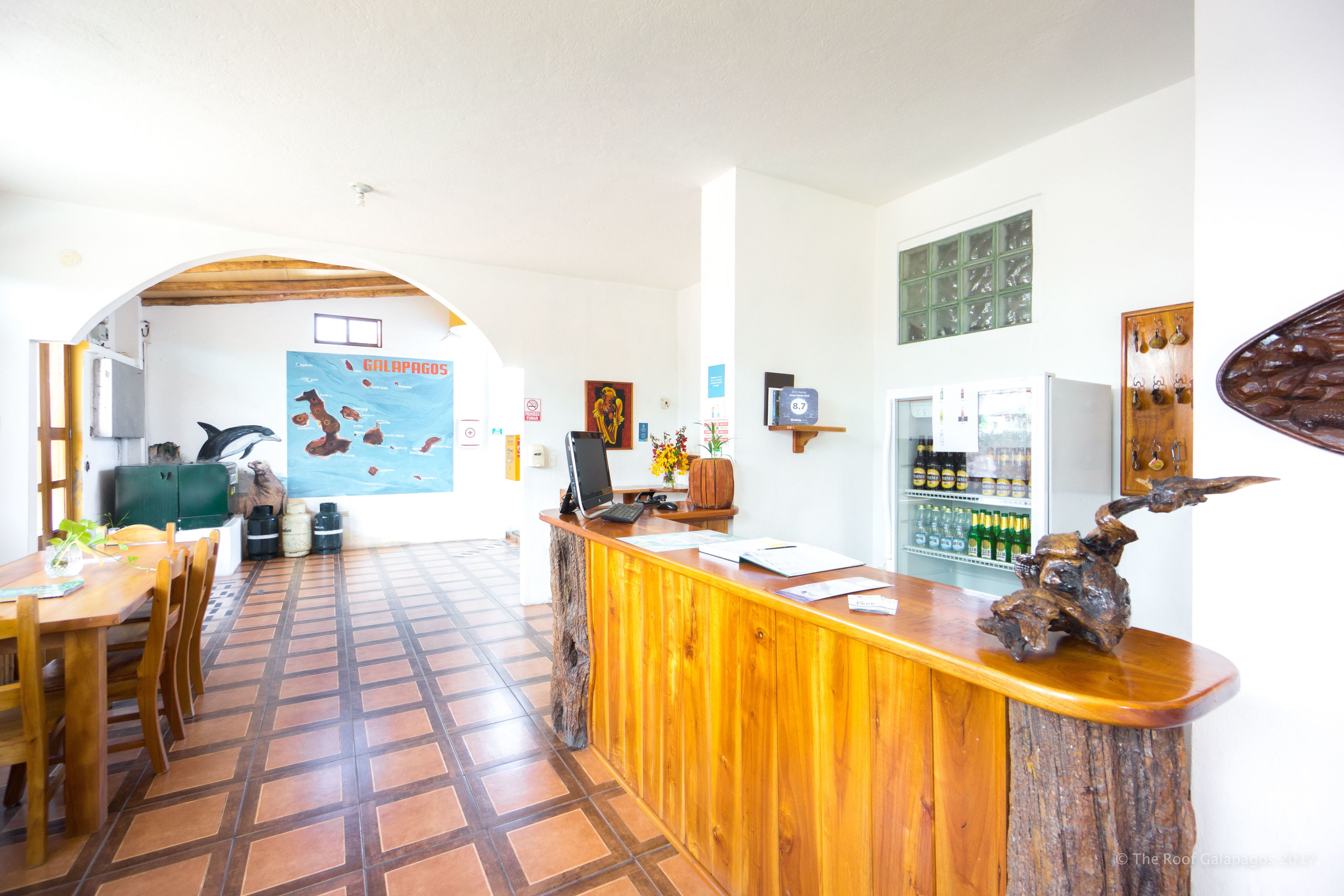 Un área de recepción con mostrador de madera, un mural, un refrigerador lleno de bebidas y piso de baldosas.