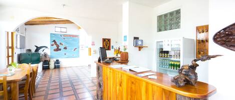 Un área de recepción con mostrador de madera, un mural, un refrigerador lleno de bebidas y piso de baldosas.
