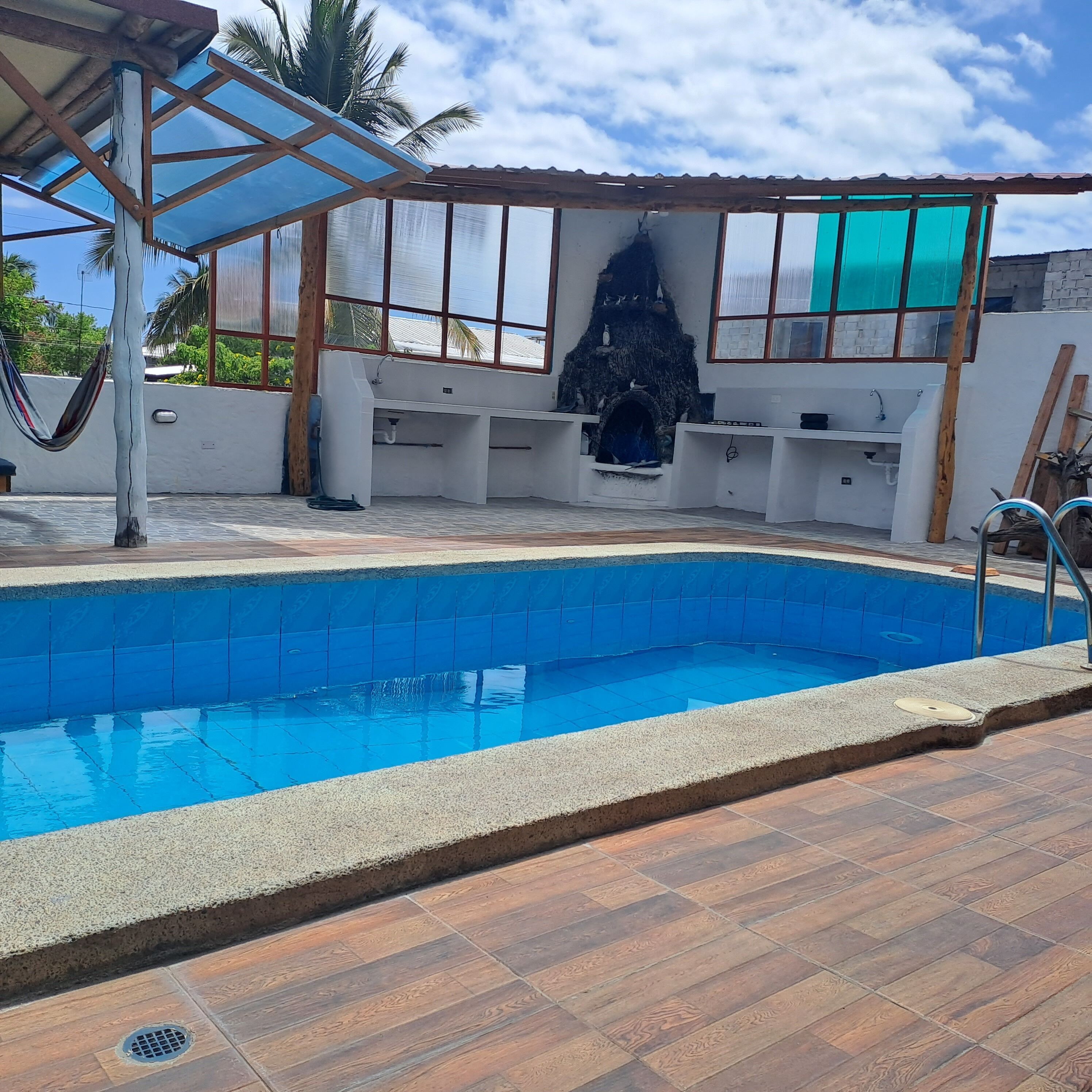 A swimming pool with a tiled deck, a covered seating area, and a stone wall with a built-in fireplace.