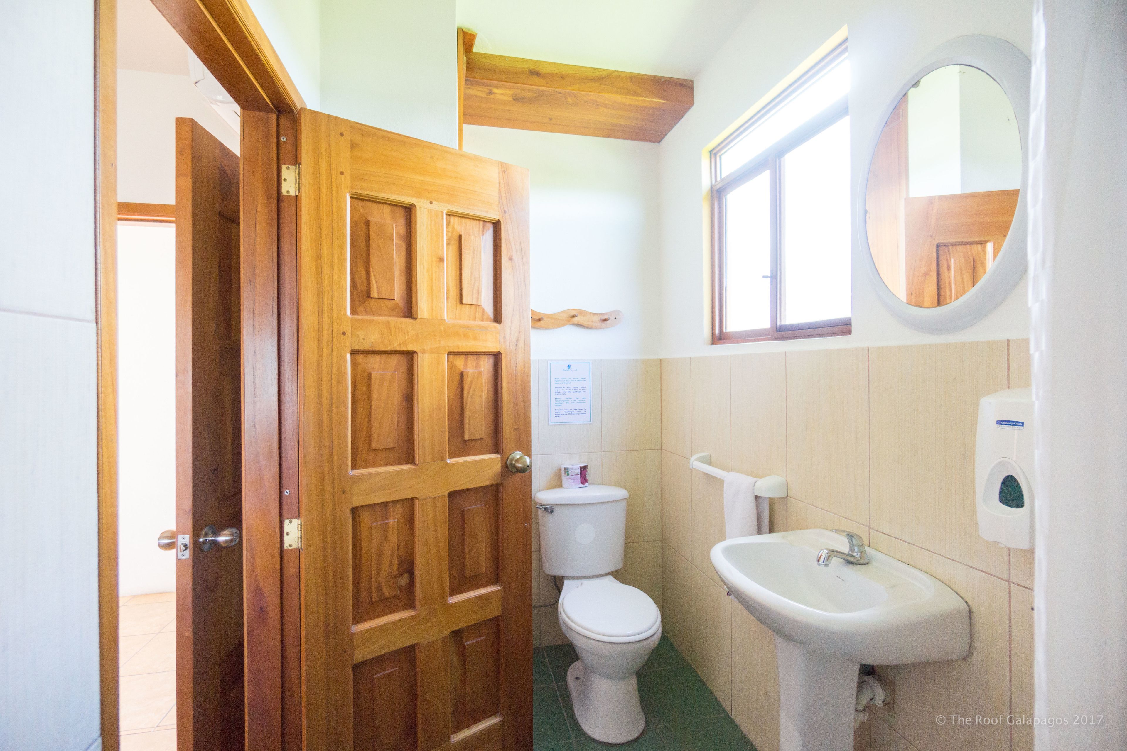 Baño con puerta de madera, inodoro, lavabo y espejo.
