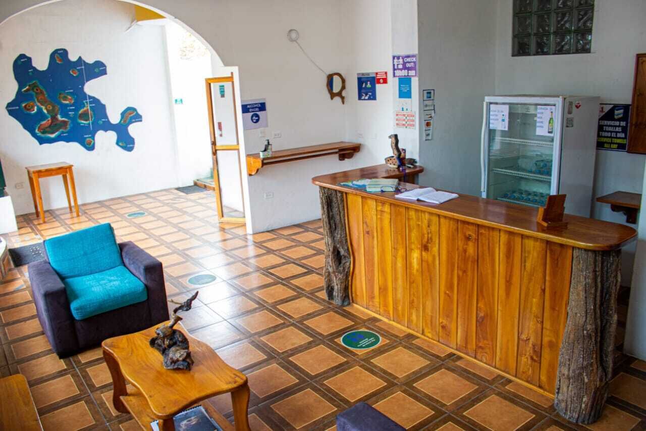Un área de recepción con mostrador de madera, un sofá azul, una pequeña mesa con un objeto decorativo y un mapa en la pared.