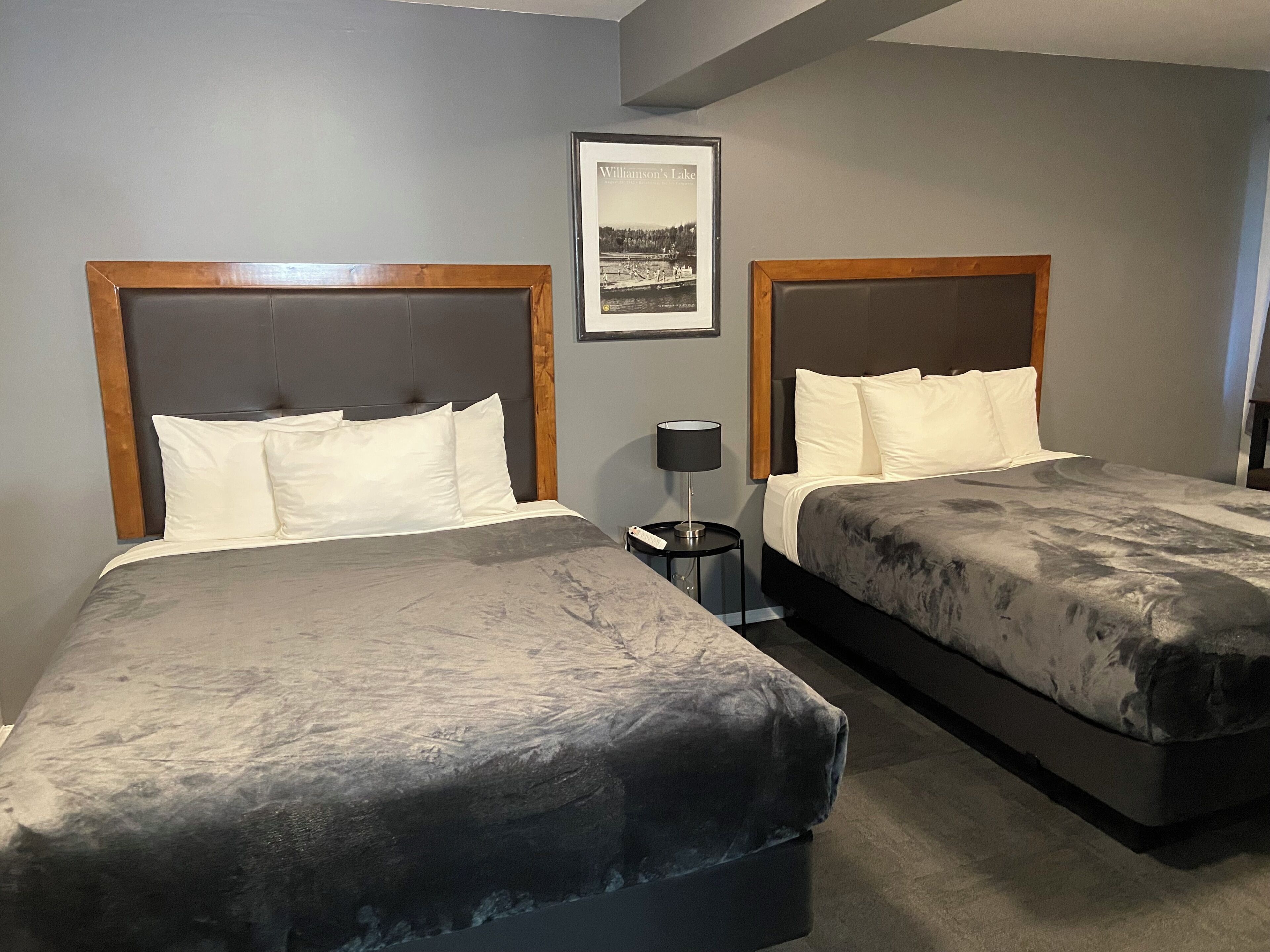 Una habitación de hotel con dos camas, un cuadro en la pared y una mesita de noche con una lámpara.