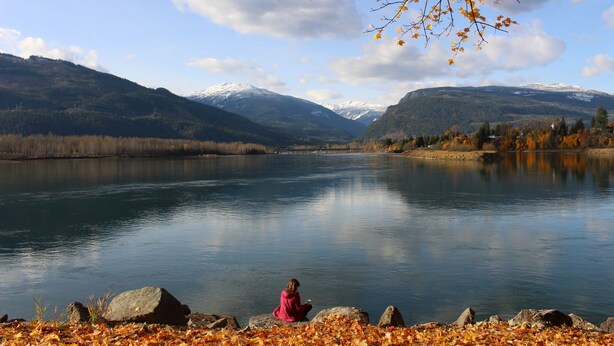 A person sitting by a calm lake with mountains in the background. - Monashee Lodge (Revelstoke)