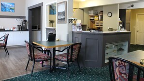 A hotel lobby with a reception desk, chairs, a coffee machine, and a clock on the wall. - Monashee Lodge (Revelstoke)