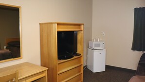 A hotel room with a wooden TV stand, a small white refrigerator, a microwave, a wooden desk, and a mirror. - Nights Inn (Thunder Bay)