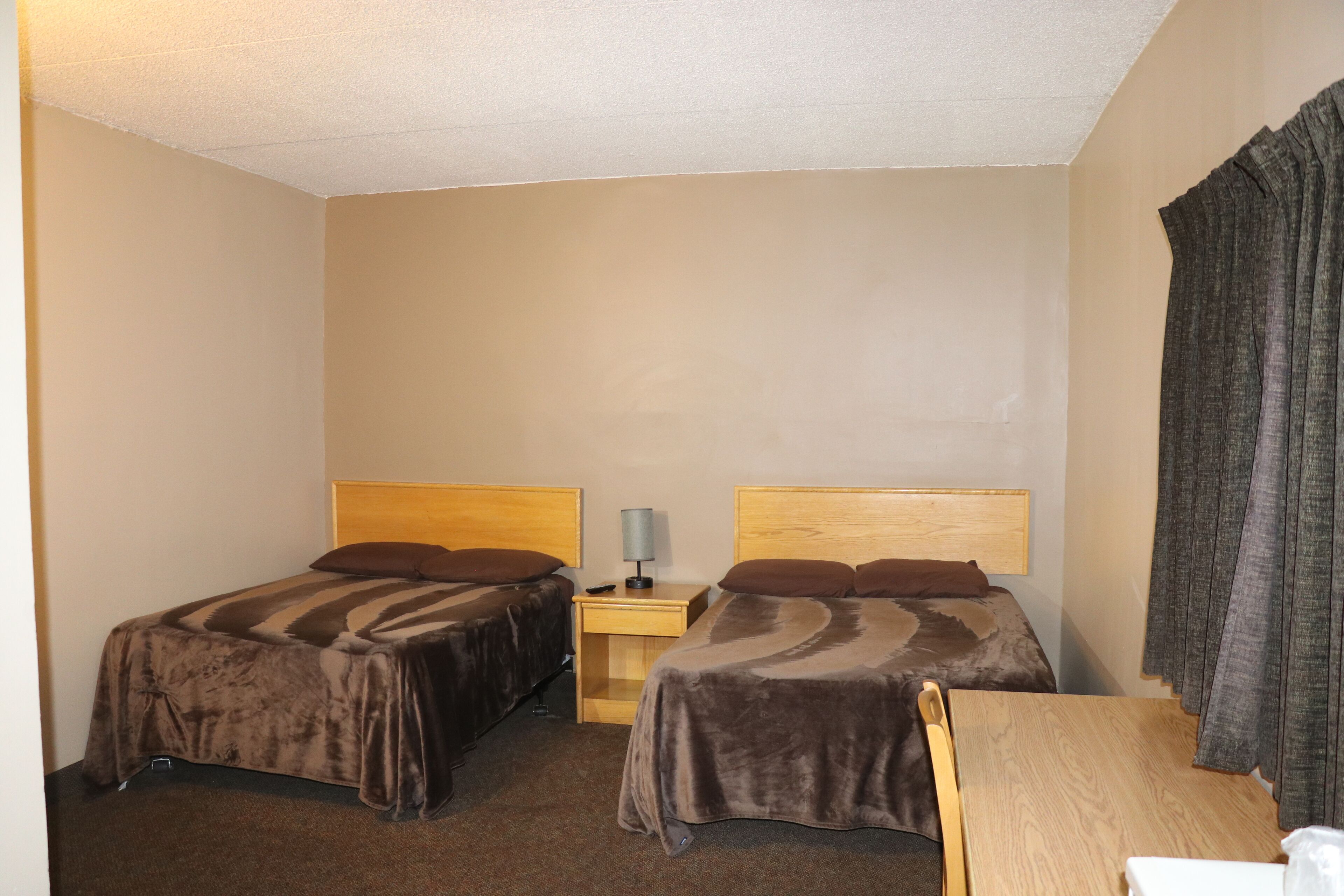 A hotel room with two beds, a wooden nightstand, a table, and a chair.