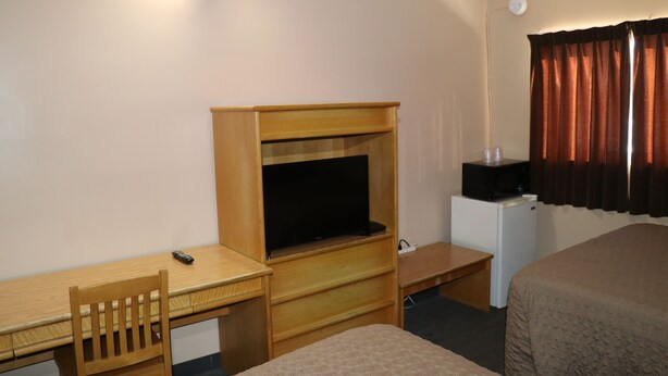 A hotel room with a wooden desk, a television, a small refrigerator, and a bed. - Nights Inn (Thunder Bay)