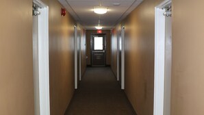 A long, narrow hallway with beige walls and carpeted floors, leading to a door at the end. - Nights Inn (Thunder Bay)