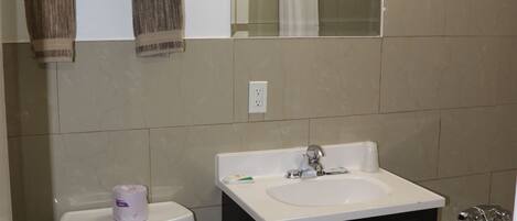 A bathroom with a toilet, sink, and bathtub. There is a towel rack above the toilet and a mirror above the sink.