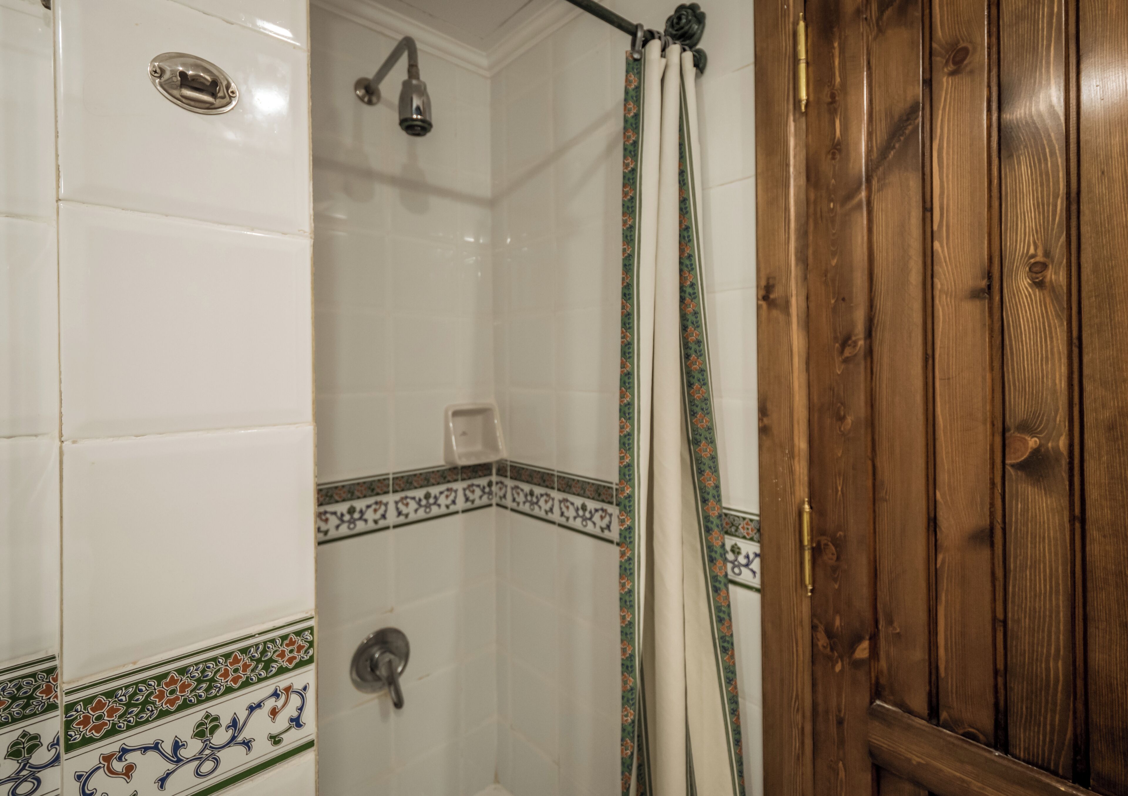 Une salle de bain avec des murs carrelés de blanc, une douche avec un pommeau de douche, des toilettes et une porte en bois.