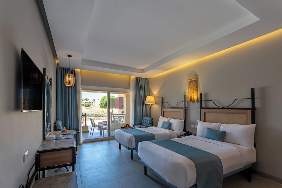 A hotel room with two beds, a desk, a TV, and a balcony with a view.