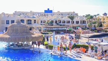 A pool area with a thatched-roof structure, lounge chairs, and a building with multiple balconies in the background.