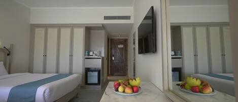 Een hotelkamer met een bed, een bureau met een schaal fruit, een televisie en een kledingkast.