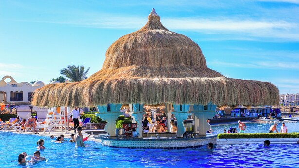 Una piscina con una estructura de techo de paja, sillas de descanso y un tobogán.