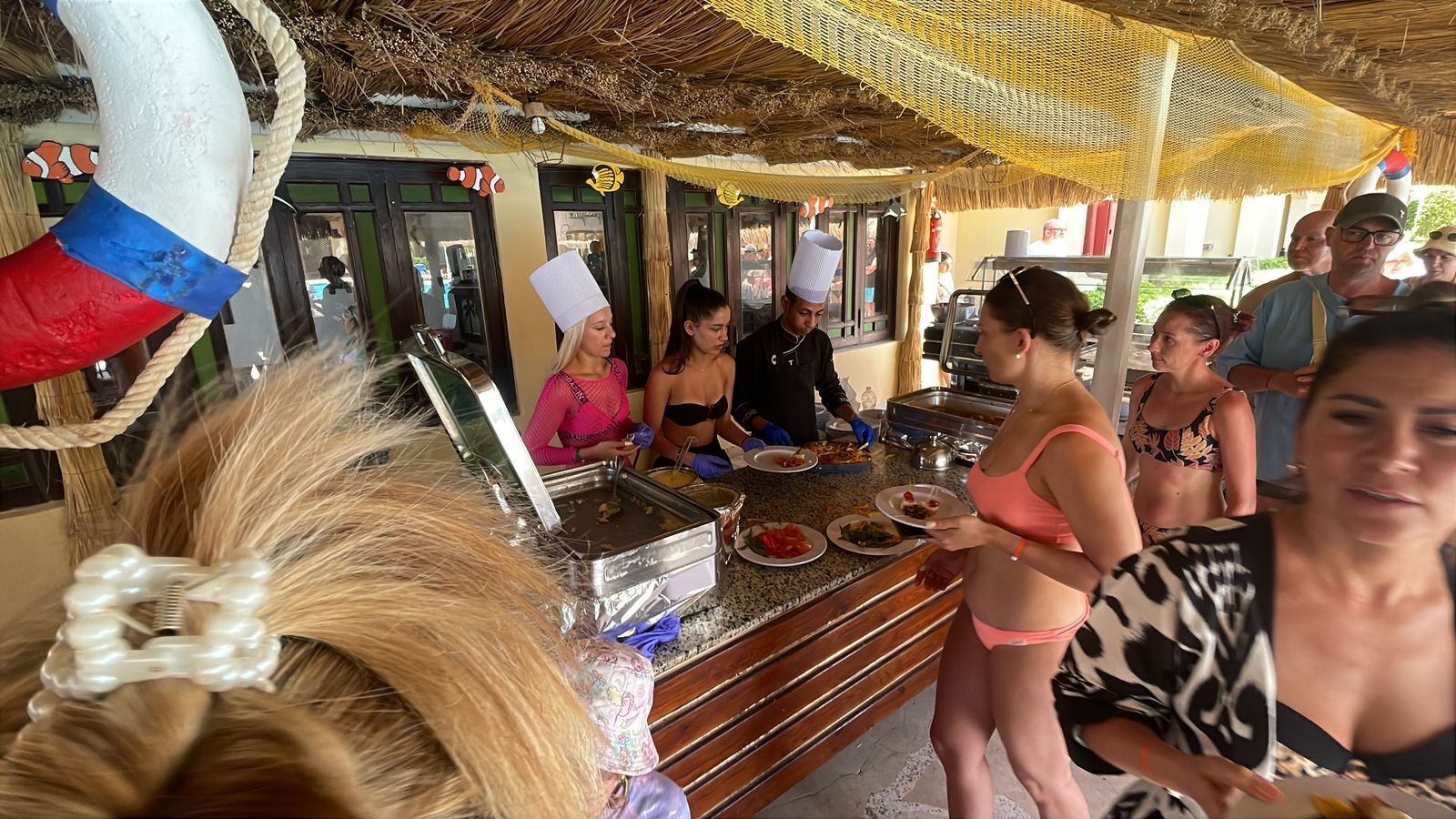 Un buffet avec différents plats et du personnel pour servir les clients.