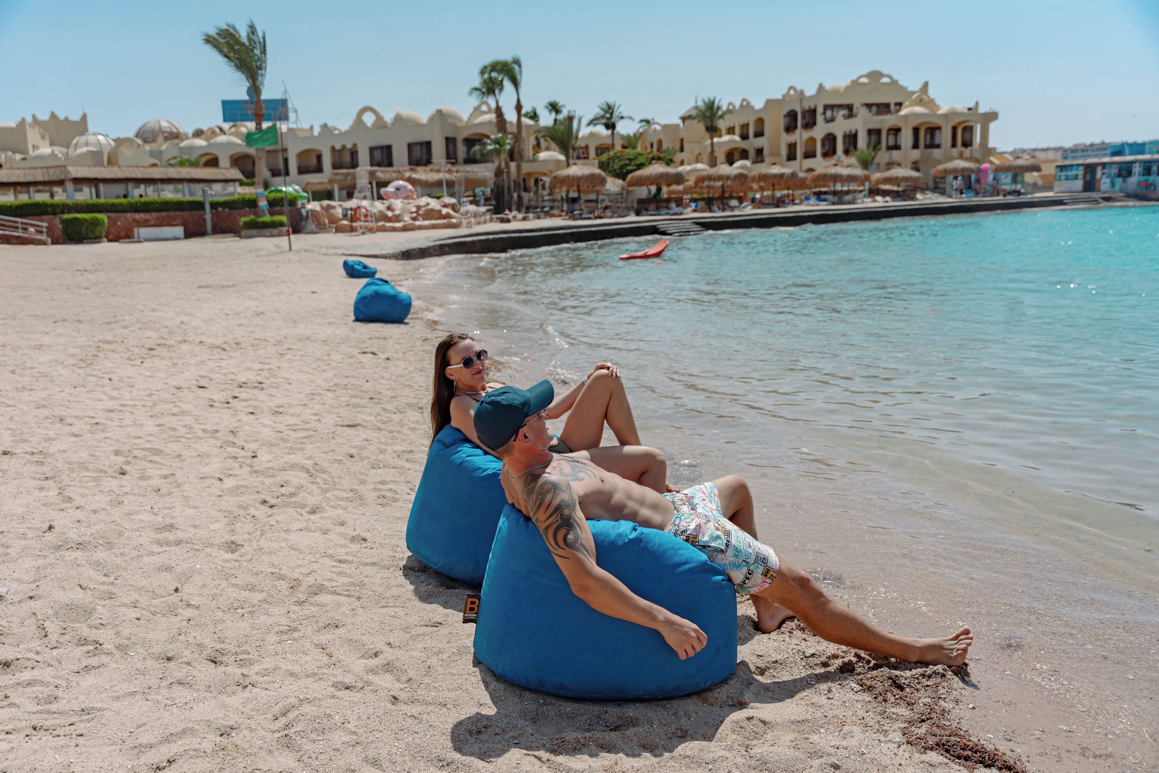 Una playa con sillones tipo puffs, una piscina y un edificio de resort al fondo.