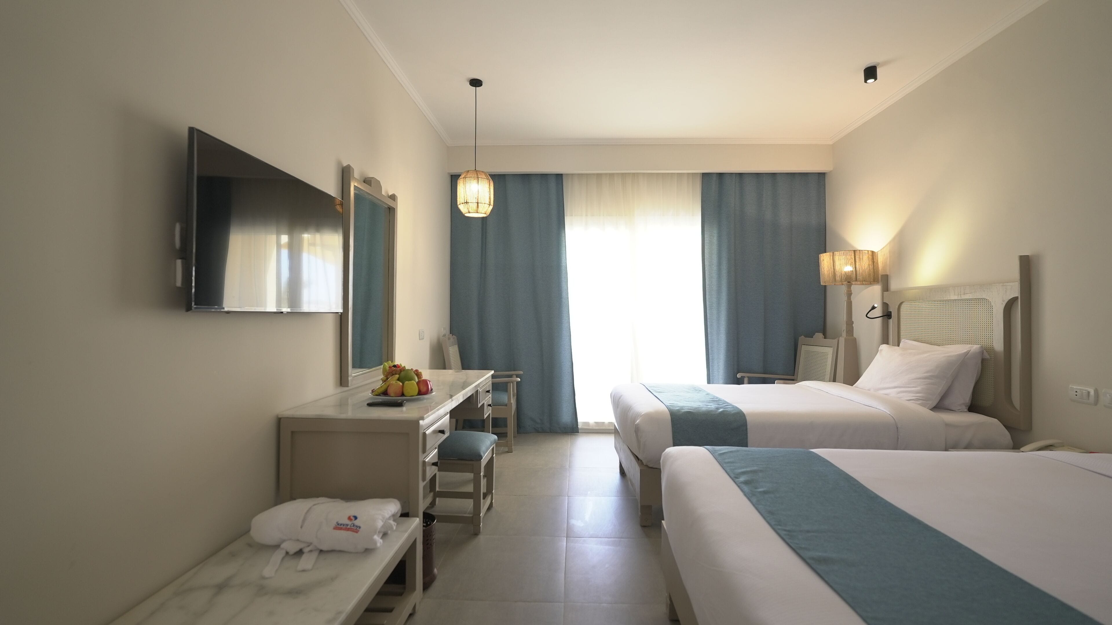 Una habitación de hotel con cama, escritorio, silla, televisor y ventana con cortinas.