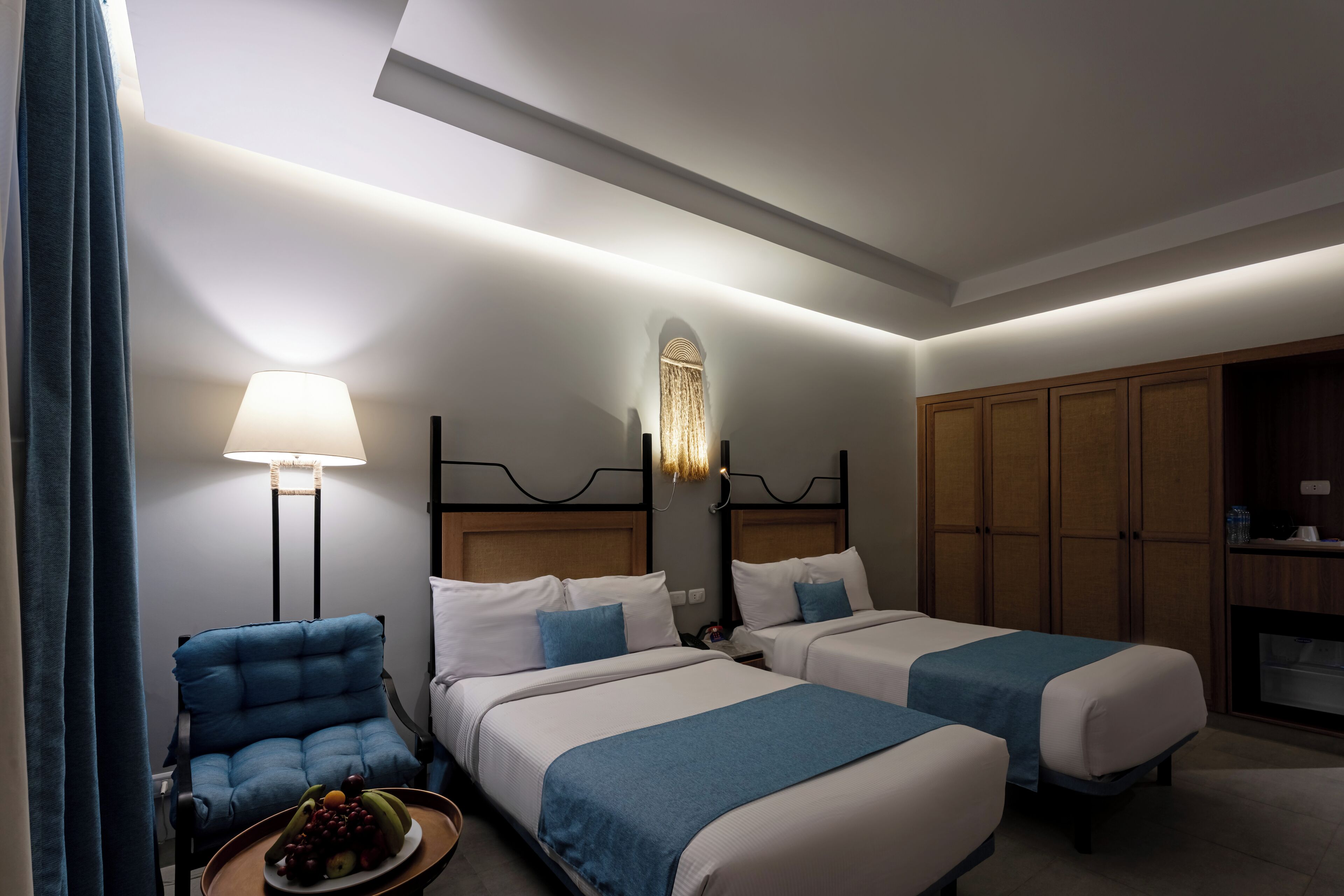 Habitación de hotel con dos camas, una silla, una lámpara y un armario.